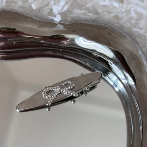 Detail of silver brushed metal hair clip with delicate beaded bow on a mirror tray