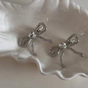 Barrettes à cheveux argentées avec nœuds, strass et cristaux en cœur sur un plateau coquille