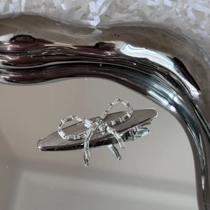 Close-up of a silver bow hair clip with rhinestones on a mirror metal tray
