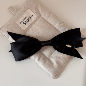 Detailed close-up of a black satin bow hairclip featuring a small metallic logo tag
