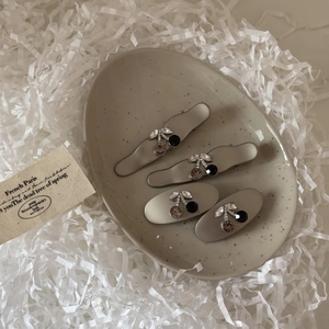 Detail of four matte grey hair clips with sparkling rhinestone cherry accents in a ceramic tray