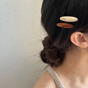 Close-up of cream and amber oval acetate hair clips with golden handmade lettering