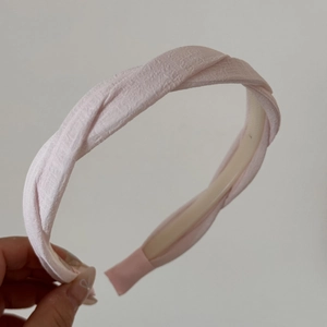 Détail d'un serre-tête en tissu plissé rose clair avec nœud torsadé et embouts antidérapants