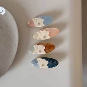 Close-up of four acetate hair clips with female profile designs and pearl accents