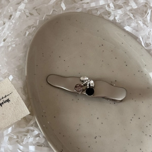 Close-up of a silver cherry hair clip with purple crystal on a ceramic gift plate