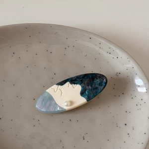 Close-up of acetic acid hair clip with profile silhouette and pearl detail