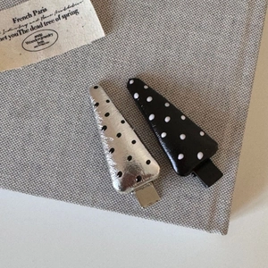 Close-up of elegant silver and black polka dot snap hair clips on a textured fabric base