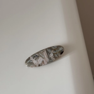 Detailed macro view of an oval acetate hair clip featuring grey marble texture and France logo