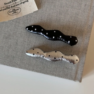 Macro detail of wave-shaped polka dot hair clips in silver and black on grey fabric
