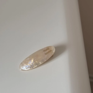 Macro detail of oval acetate hair clip in pearl white with gold handmade lettering