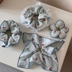 Detail of four blue cherry embroidered scrunchies and bow hair ties on a white table