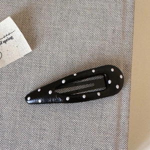 Close-up of classic black teardrop BB hair clip with white polka dot pattern on fabric