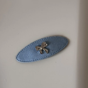Détail d'une barrette ovale en tissu bleu clair avec un nœud métallique argenté