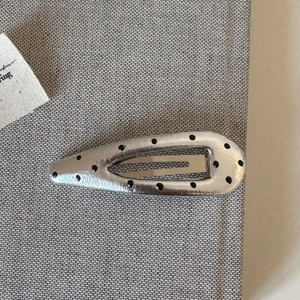 Detailed top view of a silver teardrop hair clip with black polka dots and hammered texture
