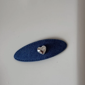 Détail de la pince à cheveux ovale en denim bleu avec emblème de cœur argenté poli