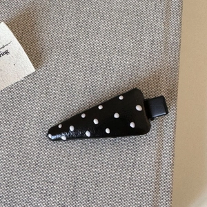Detail view of black leather triangle hair clip with white polka dots and metal duckbill clip