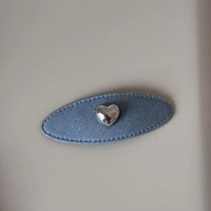 Vue détaillée de la barrette en tissu denim bleu avec un élément en forme de cœur argenté