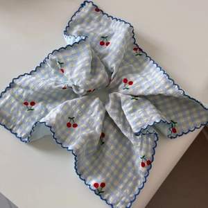 Detail of blue gingham fabric hair tie featuring red cherry embroidery and wavy edges
