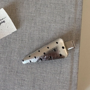 Close-up of a silver carrot-shaped hair clip with black polka dots on a grey fabric base