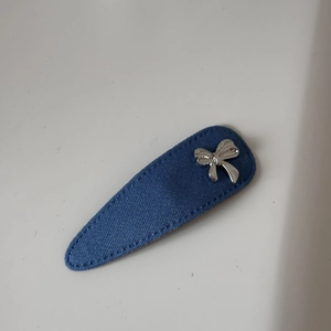 Détail d'une pince à cheveux en denim bleu avec nœud en métal argenté et coutures précises