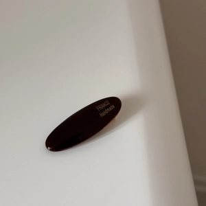 Macro detail of oval acetate hair clip with gold France Handmade lettering on dark surface