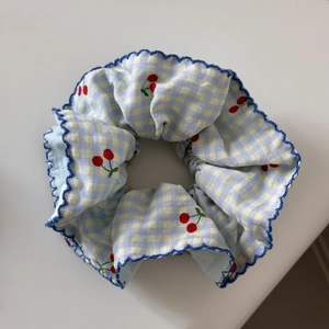 Detail of blue gingham scrunchie featuring red cherry embroidery and scalloped edges