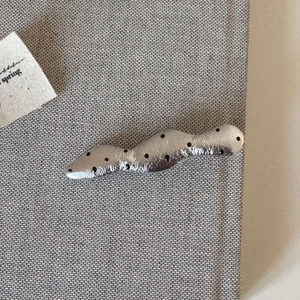 Close-up of hammered silver hair clip with black polka dots on grey fabric background