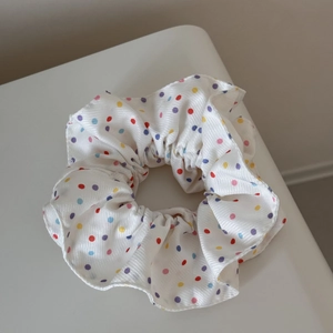 Gros plan d'un chouchou en tissu blanc à pois colorés et texture côtelée