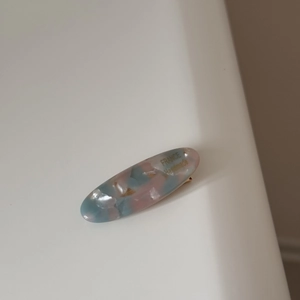 Macro detail of oval acetate hair clip with pink blue marble pattern and gold lettering