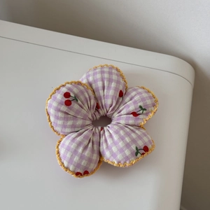 Détail d'un chouchou cerise avec bordure en dentelle jaune et motif à carreaux violets