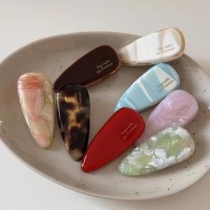 Détail de barrettes colorées en acétate en forme de goutte avec logo doré sur plateau