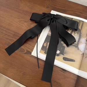 Pince à cheveux élégante avec grand nœud en satin noir posée sur un livre ancien