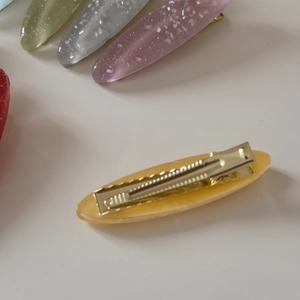 Detailed view of oval resin hair clips with sparkling finish and gold metal alligator clips