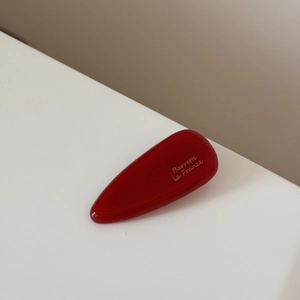 Détail d'une barrette goutte en acétate rouge avec une élégante inscription dorée
