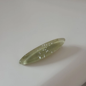 Detail of oval resin hair clip with embedded shimmering shell fragments on white background