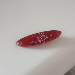 Detailed close-up of a red oval resin hair clip with fine glitter and shimmer flakes