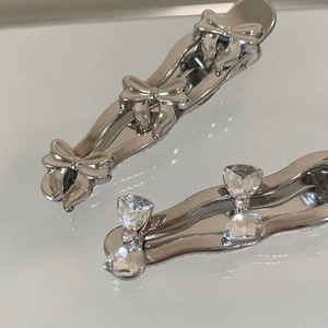 Close-up of silver bow hair clips with rhinestones on a reflective mirror background