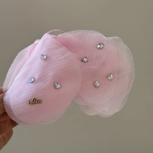 Dettaglio del fermaglio a fiocco in organza rosa con strass a cuore e ciondolo dorato