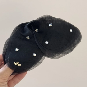 Dettaglio di un fermaglio a farfalla in tulle nero con cristalli e scritta Love