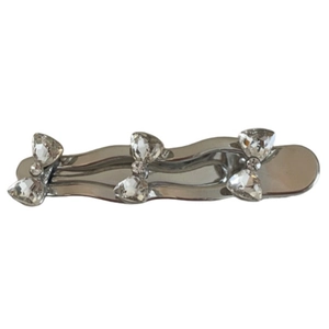 Silver wavy hairpin with three sparkling rhinestone bows on a minimalist white background