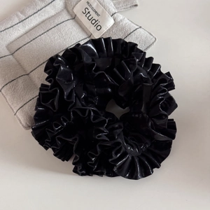 Close-up of a large black faux leather scrunchie with high-gloss pleated texture finish
