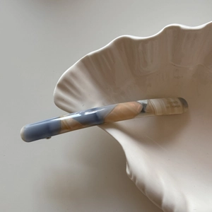 Macro detail of slim acetate barrette with blue marble texture on a white shell bowl