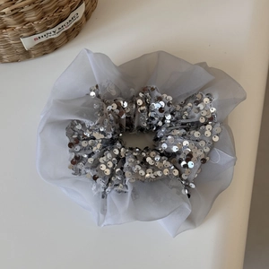 Détail d'un chouchou à paillettes argentées avec volants en organza gris et texture soyeuse