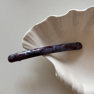Macro view of slender acetate hair clip featuring purple marbled pattern and gold logo detail
