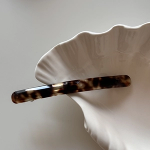 Close-up of slim tortoiseshell acetate hair clip on a white shell tray with French engraving