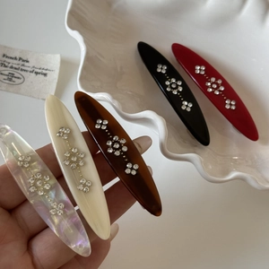 Detail of five vintage oval hair clips with sparkly rhinestone flowers on a shell tray