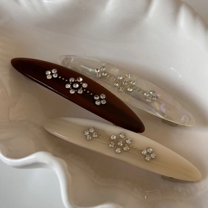 Detailed view of three vintage spring hair clips with rhinestone floral patterns on shell tray