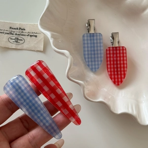 Detailed view of red and blue checkered acetate duckbill hair clips on a shell tray
