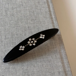 Close-up of black oval spring hair clip with sparkling rhinestone flower patterns