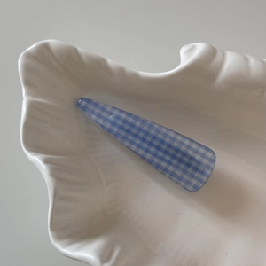 Close-up of blue and white checkered pattern hair clip on a white shell ceramic dish